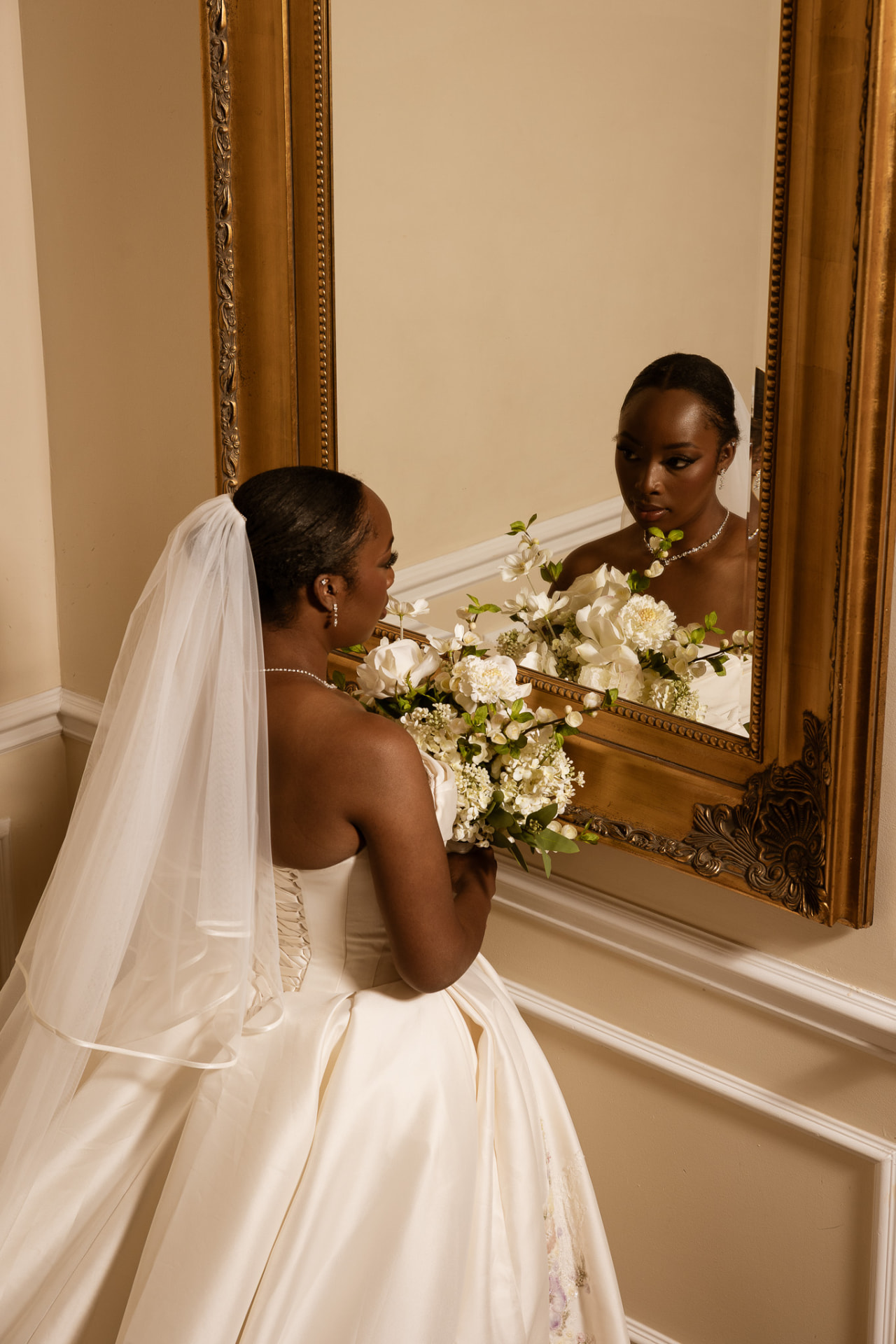 Bride looking into a gold-framed mirror with her bouquet