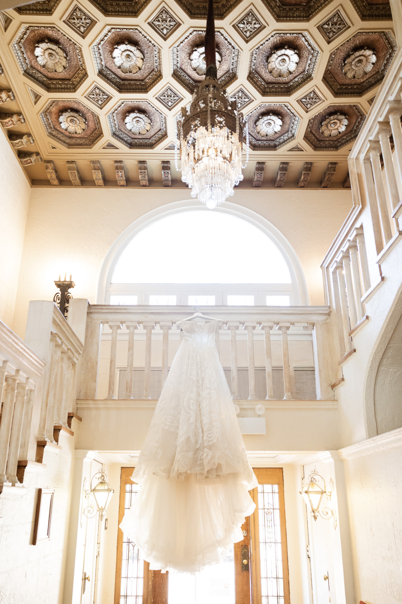 Lace ball gown hanging beneath the coffered ceiling and chandelier at The Colvin House
