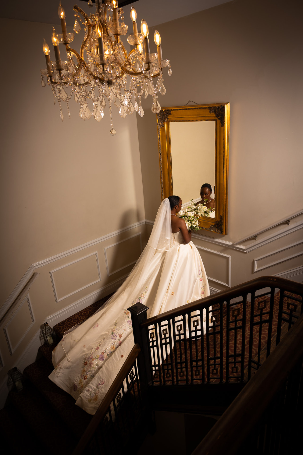 Bride on the staircase landing beneath a crystal chandelier