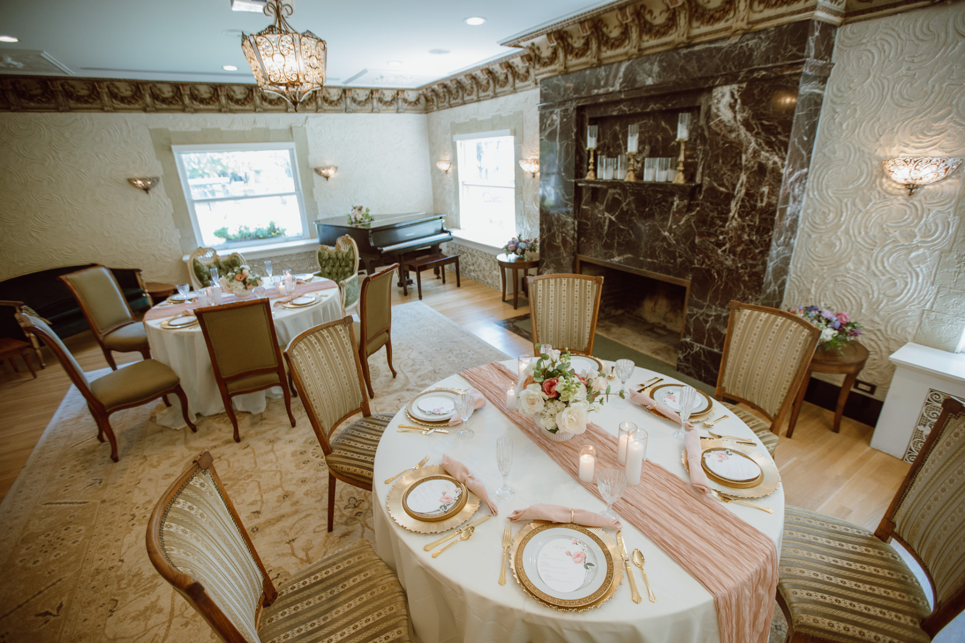 Wide view of the parlor with marble fireplace, piano, and set tables