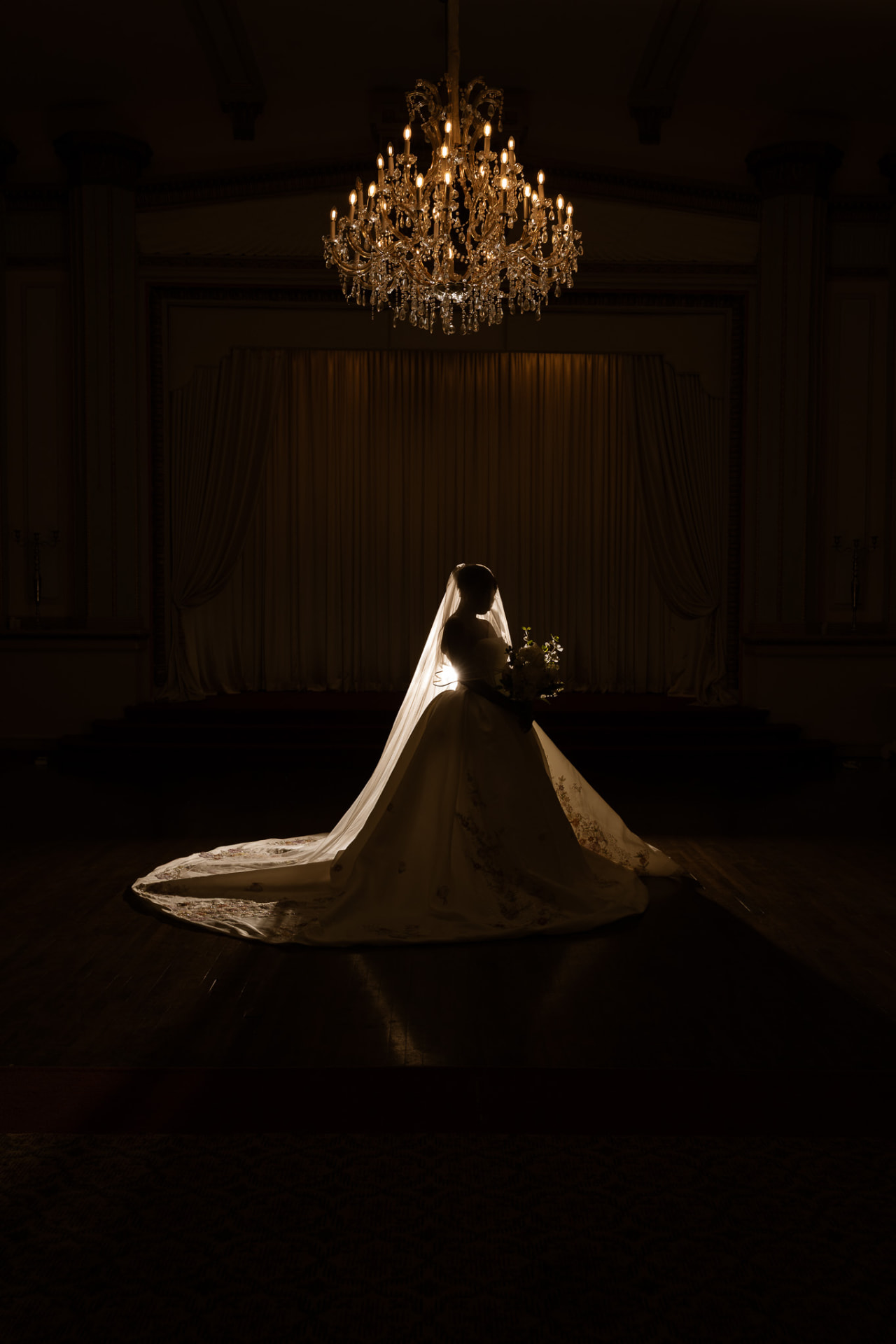 Bride alone in the ballroom under the grand chandelier