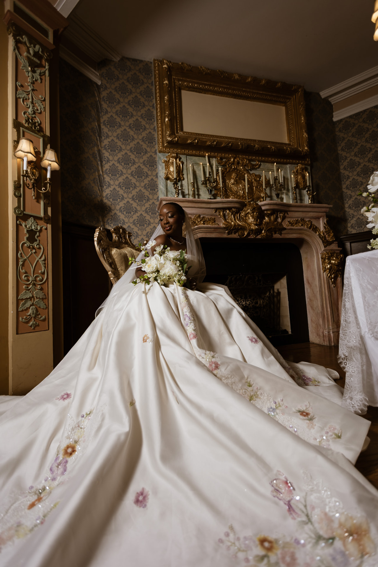 Bride with embroidered train spread before the marble fireplace